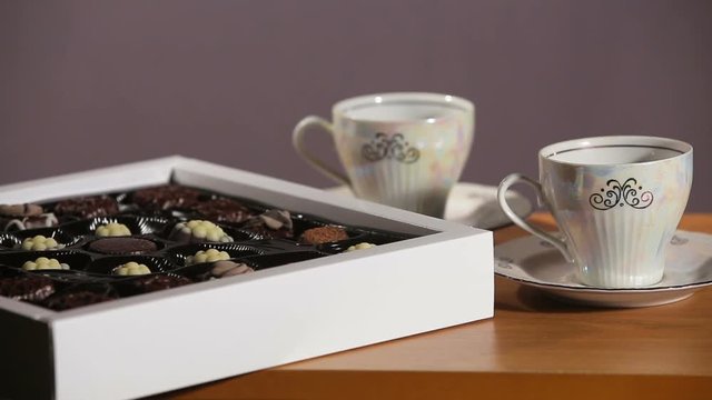 Chocolate candies and tea set on a wooden table.Cup of hot blak tea with chocolate candy.Porcelain tea set on an black background.Two teacups and teapot.Vintage tea set for two persons.