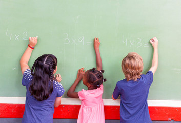 Mixed race school children writing on chalkboard