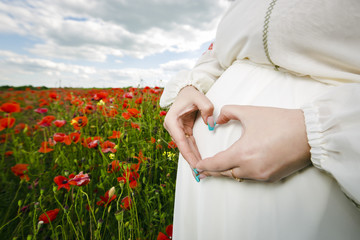 heart shaped pregancy in a flowering poppy field outdoors, close up heart shaped hands