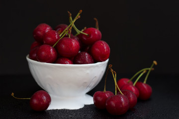 Cherry with water drops in plate on black reflective plane.