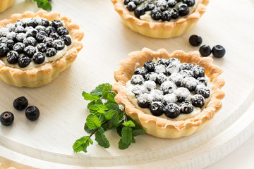 Close up of tartlets with fresh blueberries, decorated mint leaves on white wooden background. Selective focus