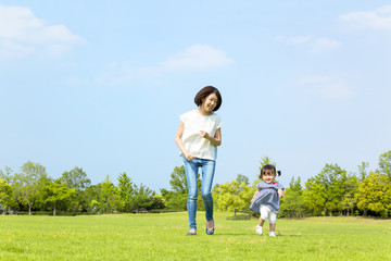 青空の下、芝生の公園で幼い女の子とt走る母子