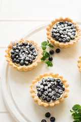 Close up of tartlets with fresh blueberries, decorated mint leaves on white wooden background. Selective focus