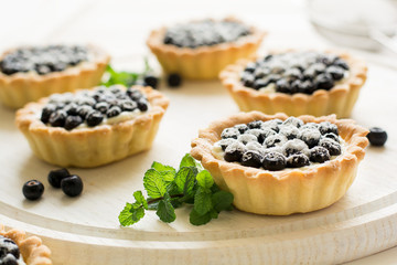 Close up of tartlets with fresh blueberries, decorated mint leaves on white wooden background. Selective focus