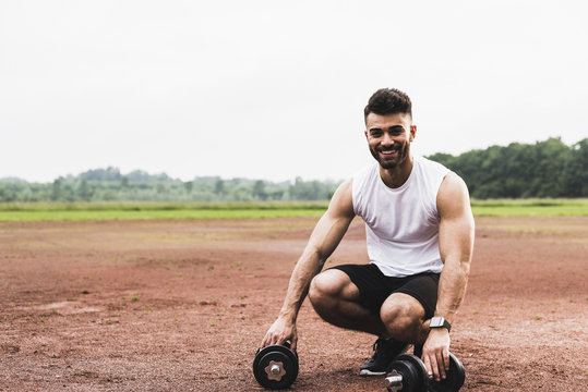 Portrait of smiling athlete with dumbbells on sports field