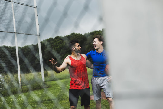 Two happy men with basketball leaving sports field