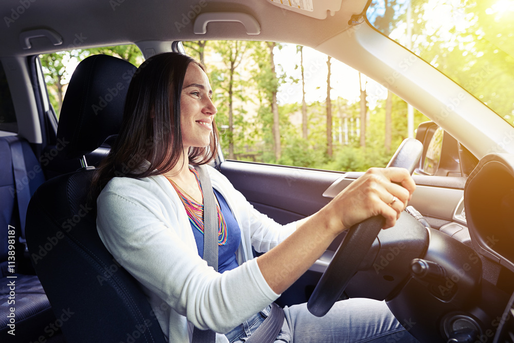 Wall mural smiling beautiful woman driving a car with seat belt fastened