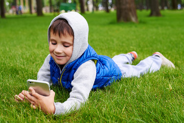  Small boy lying on green grass with smart phone