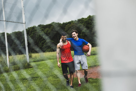 Two happy men with basketball leaving sports field