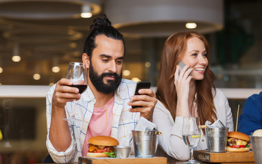 happy friends with smartphones at restaurant