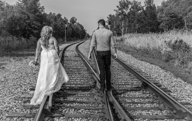 Newlywed couple walking on the rails of a pair of railroad tracks in black and white.