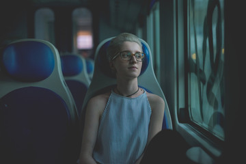 Young beautiful woman sitting on a train, looking out the window, pensive - serious, thoughtful,...