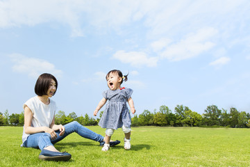 青空の下、芝生の公園で幼い女の子と遊ぶお母さん