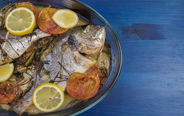 Baked fish with carrot,lemon and greenery.From above. The wooden table is blue.