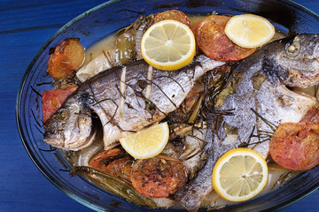 Baked fish with carrot,lemon and greenery.From above. The wooden table is blue.