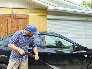 Man washing his black car near house.