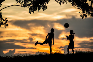silhouette of boy kick the ball at sunset