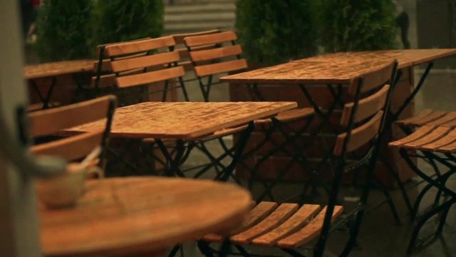 Slow motion shot of street cafe wooden tables in summer rain