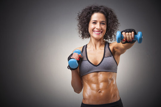 Fit woman training with dumbbells on grey bakground