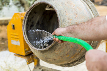 Obraz premium Worker is washing a cement mixer with a green hose pipe