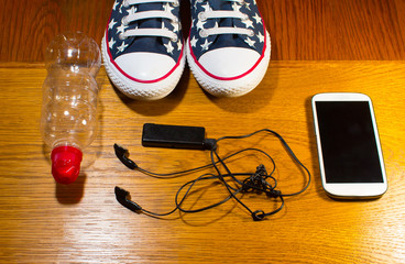 Sport shoes, water, earphone and phone on wooden background