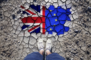 Point of view of a man standing on cracked soil with United Kingdom and European union flags.