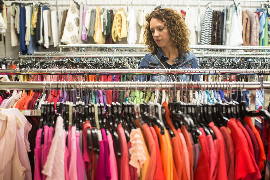 Female Shopper In Thrift Store browsing through colourful  dresses 