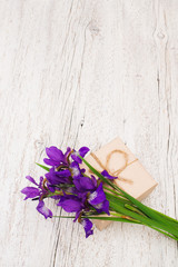bouquet of purple flowers irises and gift on a light wooden background. vertical photo. shallow depth of field