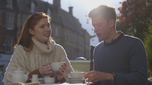 Young couple enjoying a cup of tea together in a cafe. They are sitting outdoors.