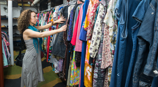 Female Shopper In Thrift Store browsing through vintage dresses