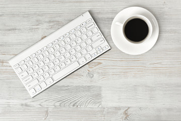 Workplace with cup of coffee and keyboard on wooden surface in top view.