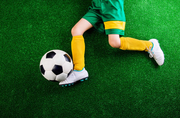 Unrecognizable little football player against green grass, studi