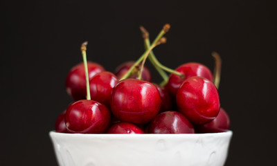 Cherry in white plate on black background.