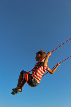 Little boy on a swing against blue sky. Background with copy space
