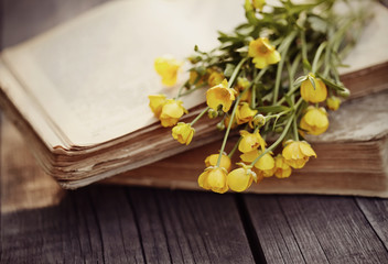 Old book and bouquet of buttercups on a wooden table.