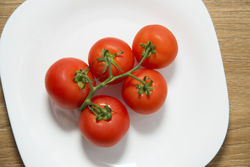 Fresh red tomatoes in white plate on wooden table