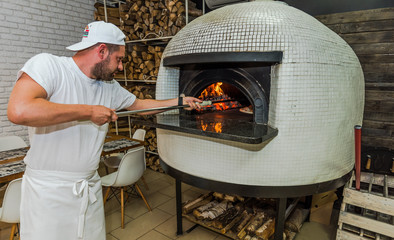 Young kitchen chef check pizza in oven