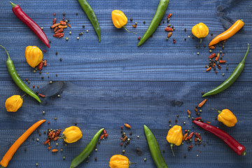 Colorful cayenne chilli peppers, yellow habanero peppers, pepperoncini peppers and color pepper on blue wooden table with copyspace in the centre. Top view.