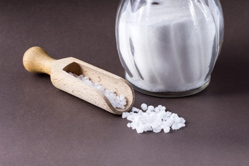 salt crystals with wooden spoon and glass salt shaker on brown background