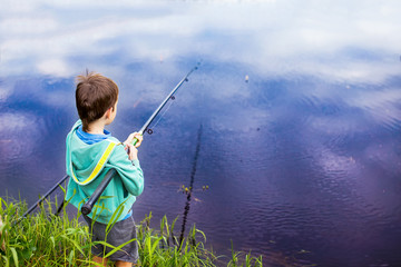 boy with a fishing rod standing by the water. young fisherman on a fishing trip. back view. copy space for your text