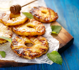 Grilled fruit pineapple slices with addition of honey on a blue wooden table