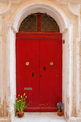 Old shabby wooden red door with stained glass. Potted flowers - hyacinth and narcissus. Mdina, Malta.