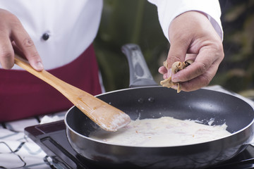 Chef putting mushroom to the pan cooking spaghetti carbonara