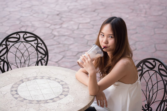 Beautiful asian girl in white dress sitting on a chair and drink