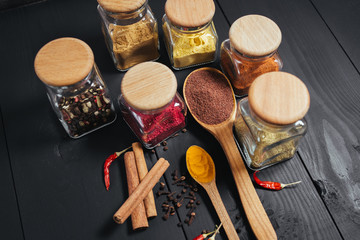 Ground spices in bottles with spon, papper, cinnamon on black wooden background. Close-up
