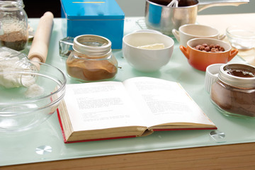 Cookbook on table ingredients cups bowls
