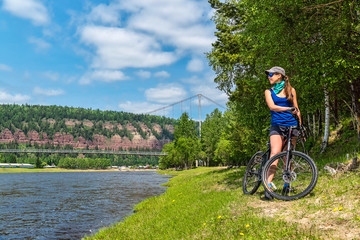 Fototapeta premium Girl with bicycle standing on river bank