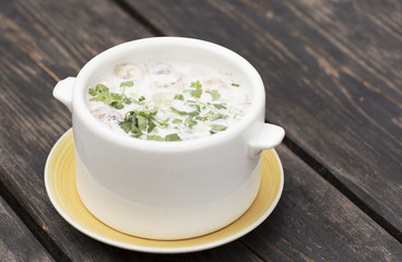 Thai soup in a white dish on a wooden table. Spicy coconut milk soup with shrimp and greens. 