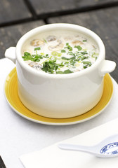 Thai soup in a white dish on a wooden table. Spicy coconut milk soup with shrimp and greens. 