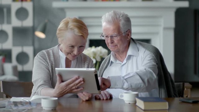 Happy lovely retired couple use tablet computer and laugh